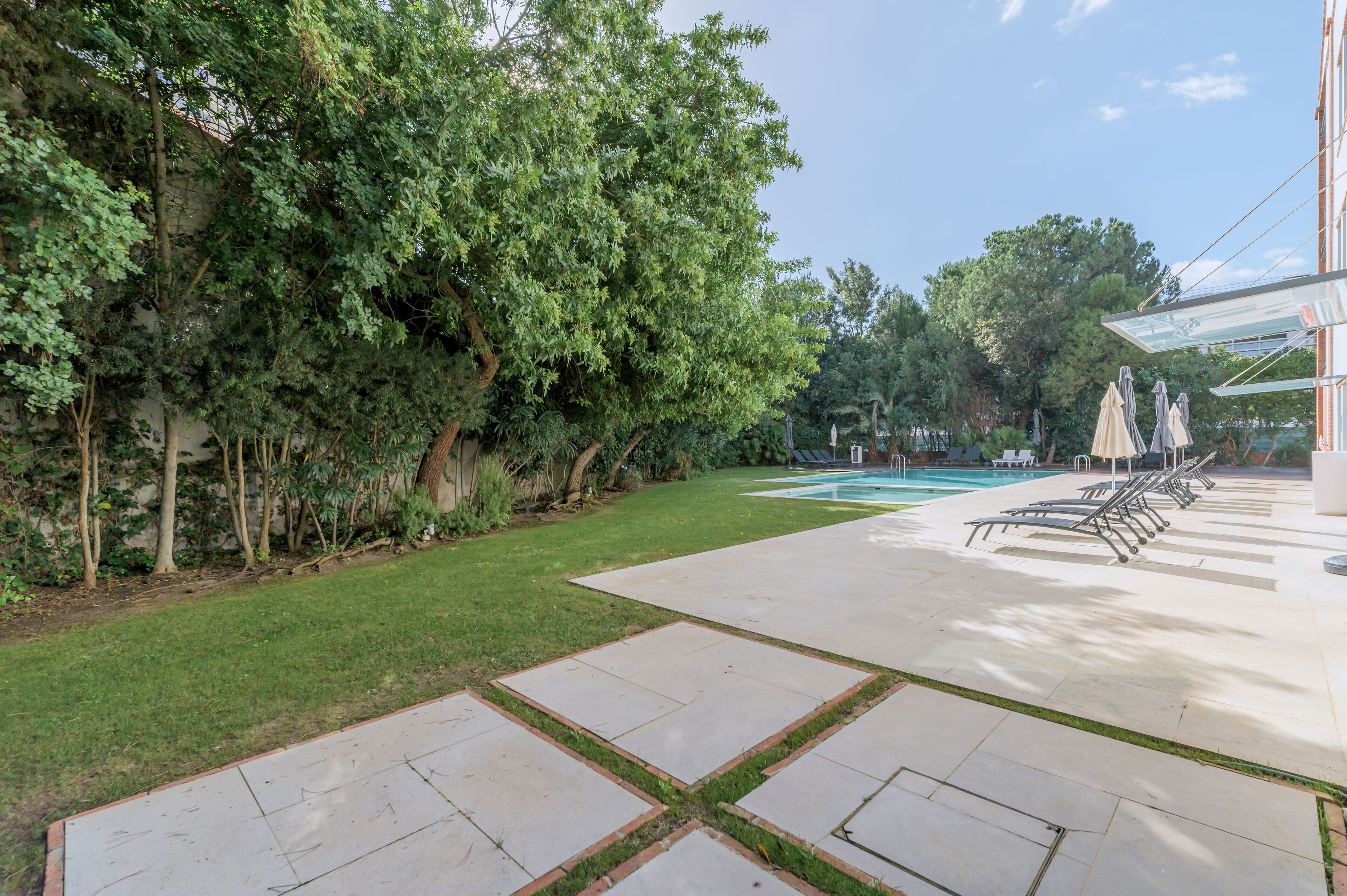 Un área de piscina con vista despejada, sillas de descanso y una terraza con suelo de baldosas.