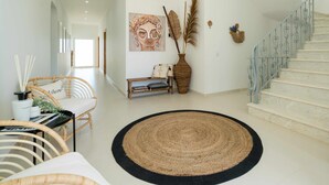 Un pasillo amplio con escaleras, un tapiz tejido, muebles de mimbre y decoración mural.