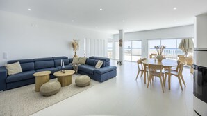 Una sala de estar moderna con un sofá azul, mesas de centro redondas y un comedor con sillas de madera.