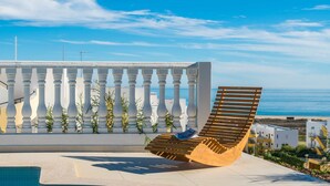Una tumbona con vista al mar, un balcón blanco y una piscina.