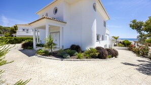 Una villa blanca con techo de tejas, un porche cubierto y un camino de entrada pavimentado.