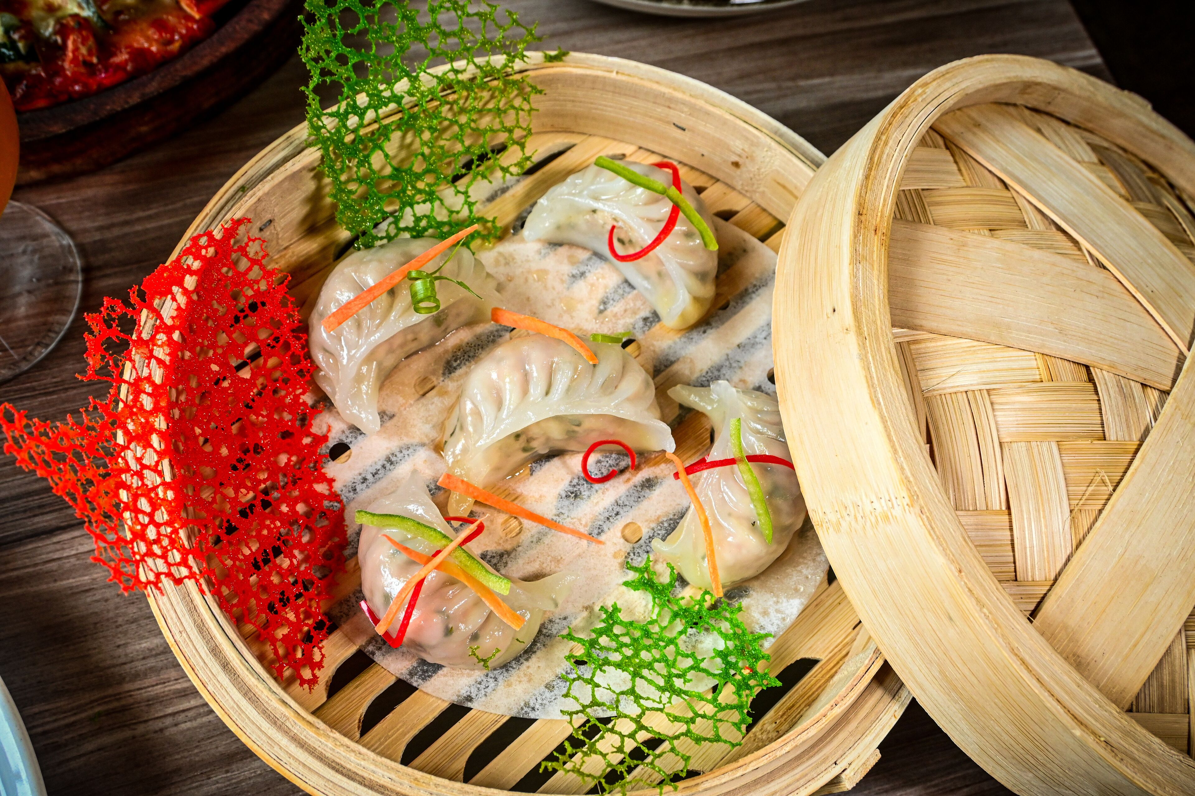 A bamboo steamer basket with dumplings, garnished with red and green vegetables.