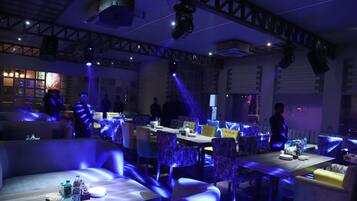 A restaurant with tables and chairs, some with blue lighting. There are people in the background.
