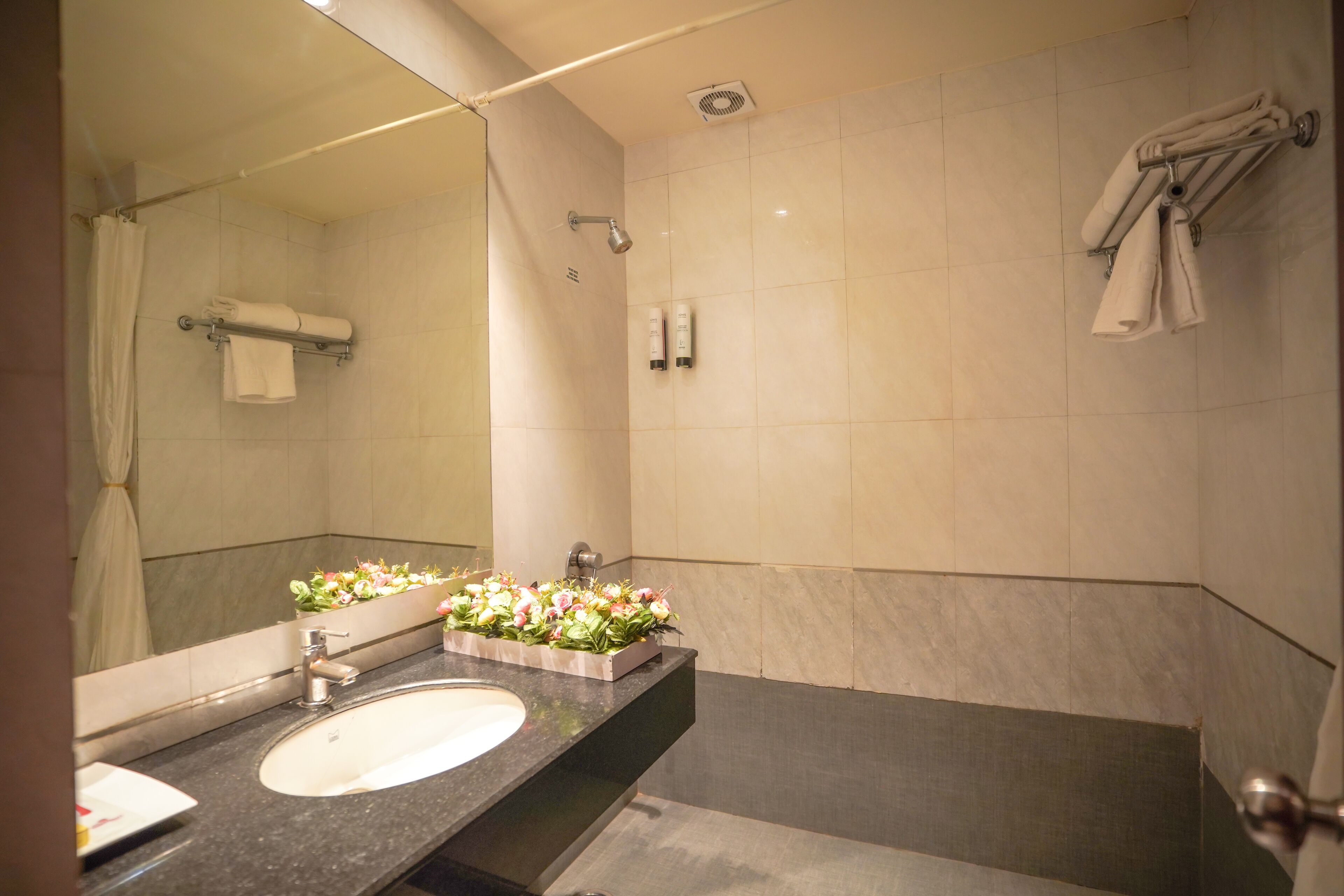 A modern bathroom with a large mirror, a sink, a shower, and a towel rack.