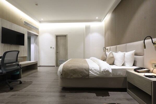 A modern hotel room with a large bed, a desk with a chair, a flat-screen TV mounted on the wall, and a bedside table with a lamp. - Hotel Swarn Towers (Bareilly)
