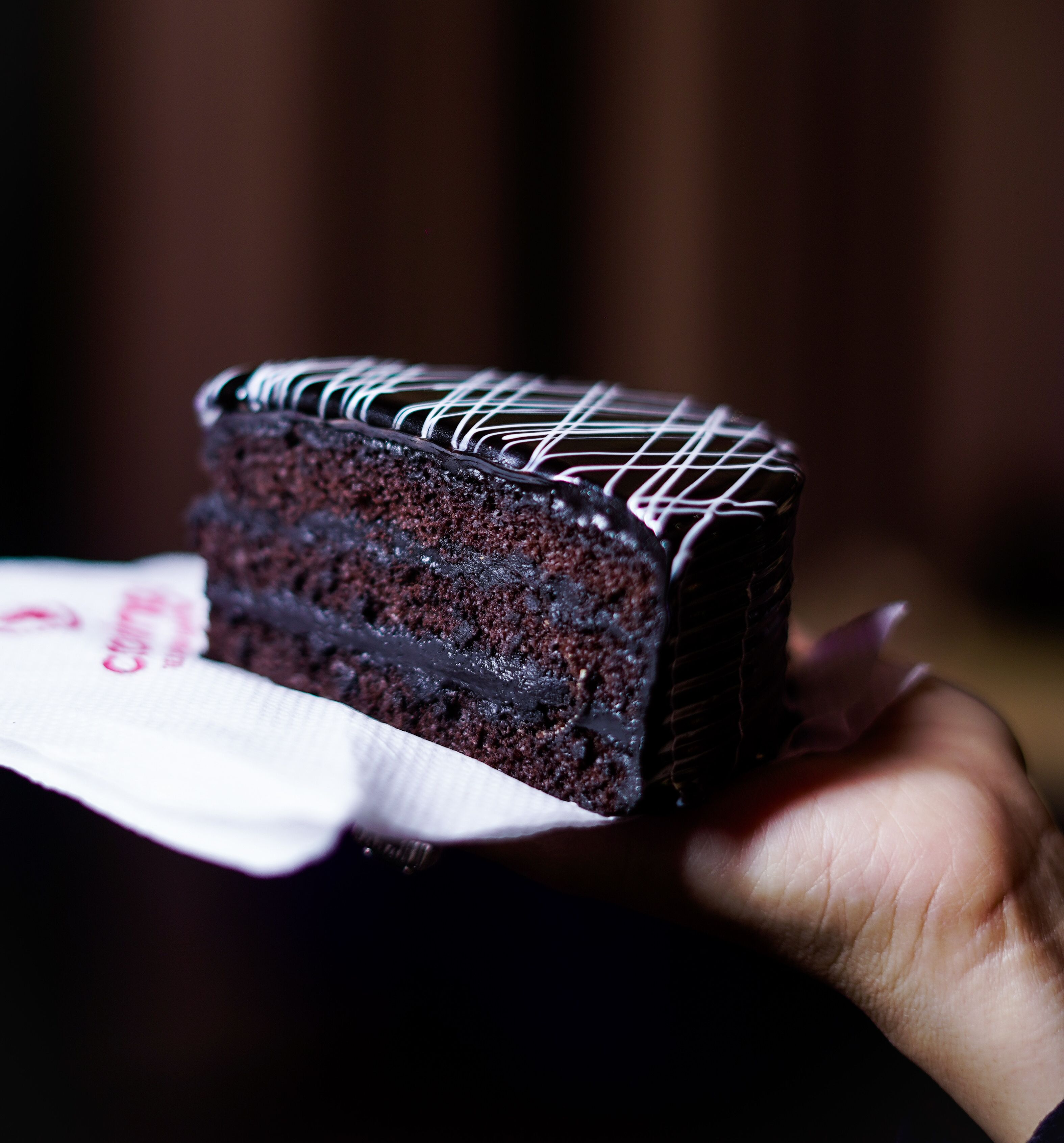 A slice of chocolate cake with white icing on a white napkin.