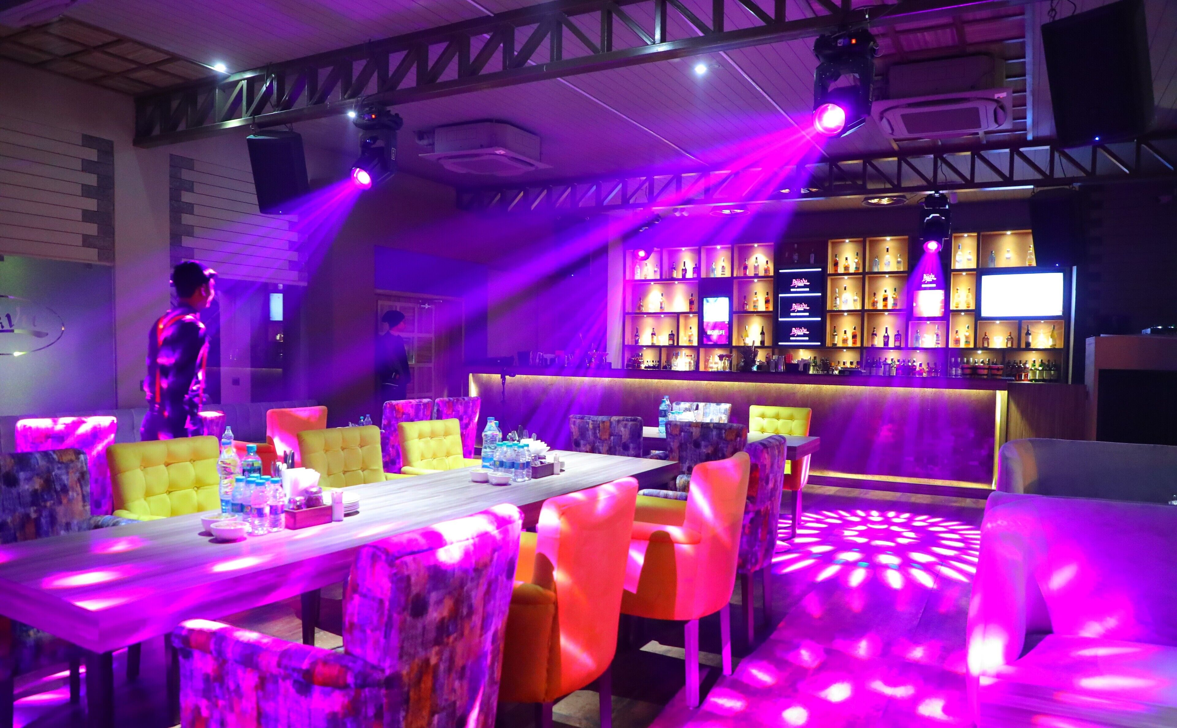 A bar area with a long counter, multiple shelves of bottles, and a variety of bar stools.