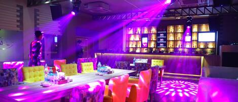 A bar area with a long counter, multiple shelves of bottles, and a variety of bar stools.