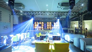A bar area with tables and chairs, a bar counter, and shelves with bottles. - Hotel Swarn Towers (Bareilly)