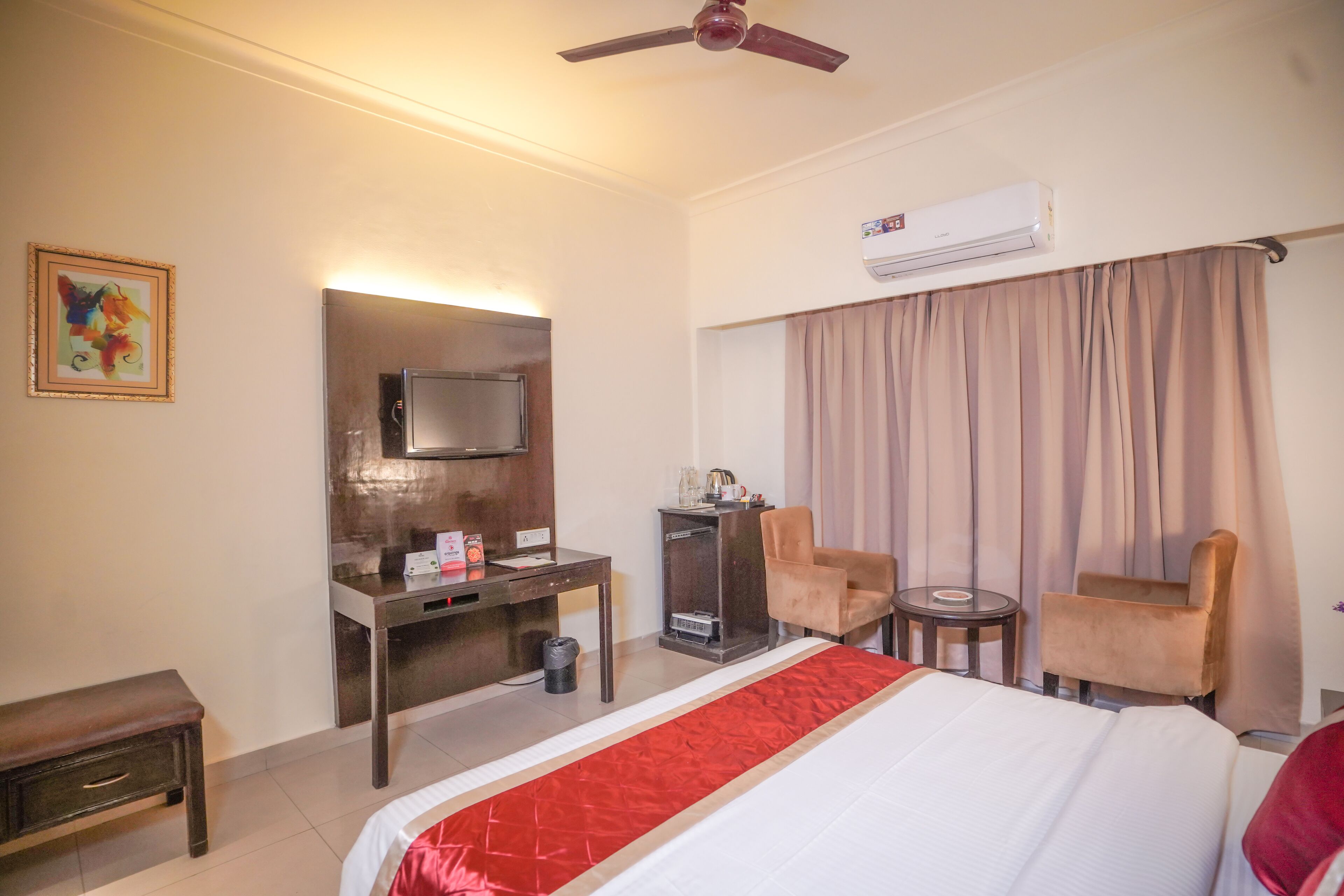 Una habitación de hotel con cama, escritorio, silla, televisor y aire acondicionado.