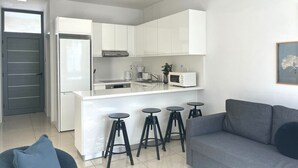 Una cocina moderna con armarios blancos, una isla central con taburetes, un sofá gris y una puerta con líneas horizontales.