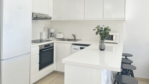 Una cocina moderna con armarios blancos, un refrigerador Bosch, una cafetera, un microondas y una pequeña planta.