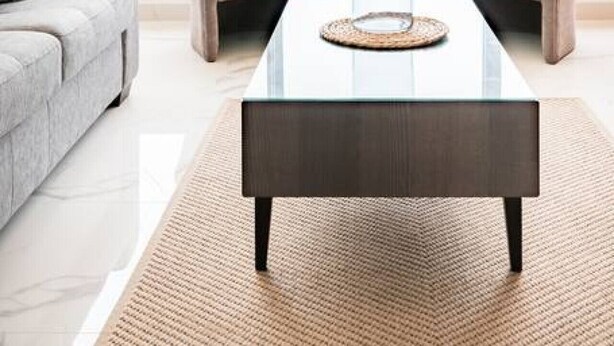 Una sala de estar moderna con una mesa de centro de vidrio, dos sillones, un sofá y vista al océano a través de ventanas amplias.