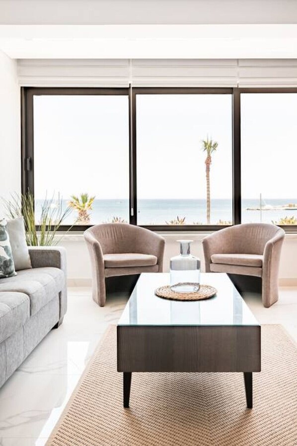 Relax in this stylish living room with a sofa, armchairs, and a coffee table, offering a view of the ocean and palm trees.