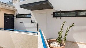 Un edificio moderno con fachada blanca, ventanas de marco negro y una puerta. Hay una planta en maceta con hojas verdes en el suelo.