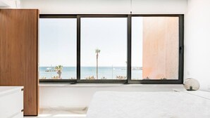 Un dormitorio con un ventanal grande que da al mar, una cama y un armario de madera.