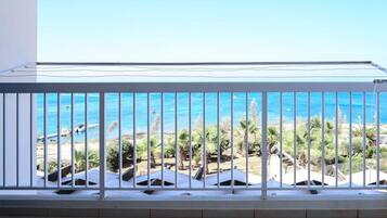 Un balcon doté d’une balustrade en métal, donnant sur une plage bordée de palmiers et surplombant un ciel bleu azur.