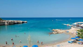Une plage avec une eau d’un bleu limpide, des gens qui se baignent et des parasols de plage.