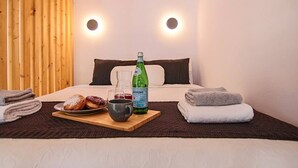 Una habitación de hotel con una cama, un panel de pared de madera, una mesita de noche con una botella de agua, un plato de pasteles y una taza.