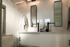 Un baño moderno con paredes de mármol, un tocador blanco, dos espejos y una toalla colgada en la pared.