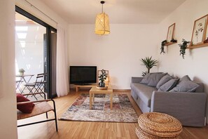 Ein Wohnzimmer mit grauem Sofa, einem Fernseher, einem Holztisch, einem gemusterten Teppich und einer Pendelleuchte.