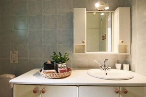Une salle de bain avec un lavabo blanc, un miroir au-dessus et un panier contenant des articles de toilette sur le comptoir.