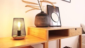 Un escritorio de madera con una lámpara, un jarrón con plantas secas y un cuadro en la pared.