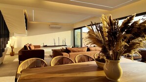 A modern living room with a wooden dining table, wicker chairs, a sofa, and a staircase. - Phaedrus Living: Venus Seaview Lighthouse Villa (Paphos)