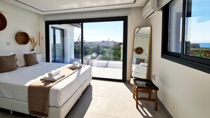A modern bedroom with a large bed, a small table, a mirror, and a view of the outdoors. - Phaedrus Living: Venus Seaview Lighthouse Villa (Paphos)