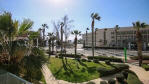 A sunny outdoor area with palm trees, a well-maintained lawn, and a building in the background. - Phaedrus Living: Seaside Modern Flat Limnaria 123 (Paphos)