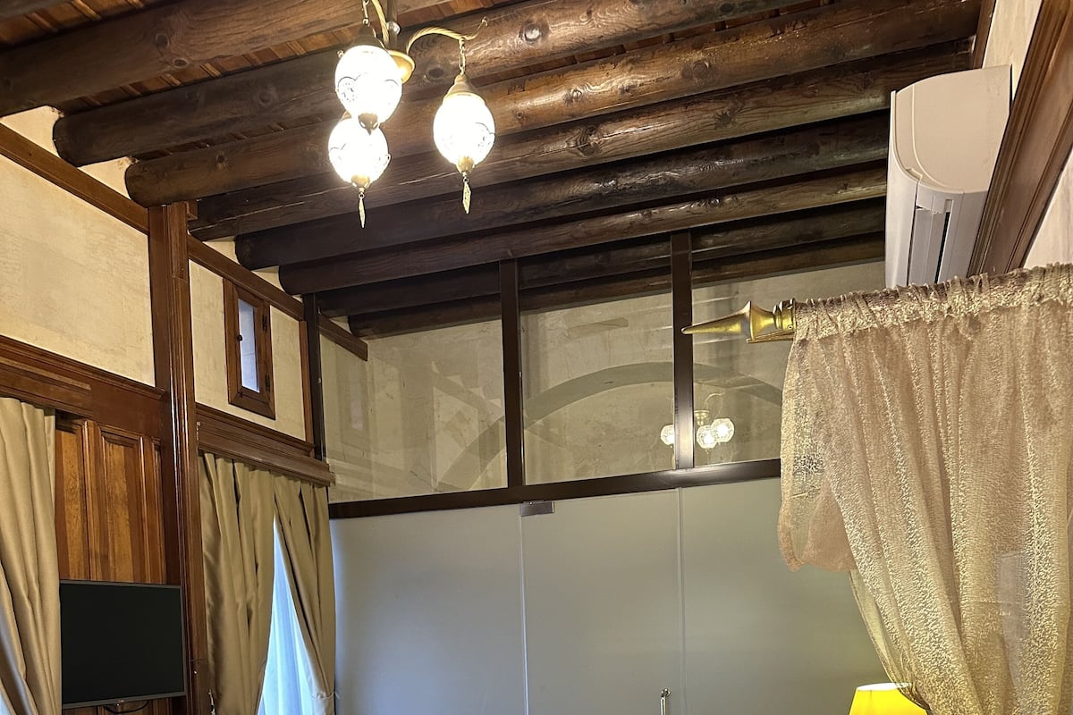 Een slaapkamer met een bed, een bedlamp, gordijnen en een houten plafond.