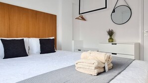 Een moderne slaapkamer met een houten hoofdbord, een bed met zwart-witte beddengoed, een nachtkastje met een vaas, en een opgevouwen handdoek op het bed.