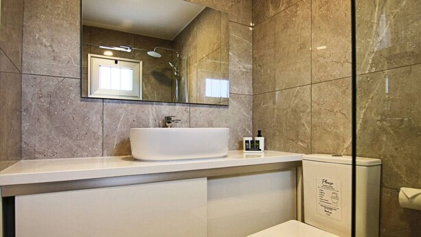 Un baño moderno con un espejo grande, un lavabo blanco y un inodoro.