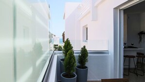 Un balcón estrecho con plantas en macetas, un banco de madera y una vista parcial de un área de cocina con taburetes.