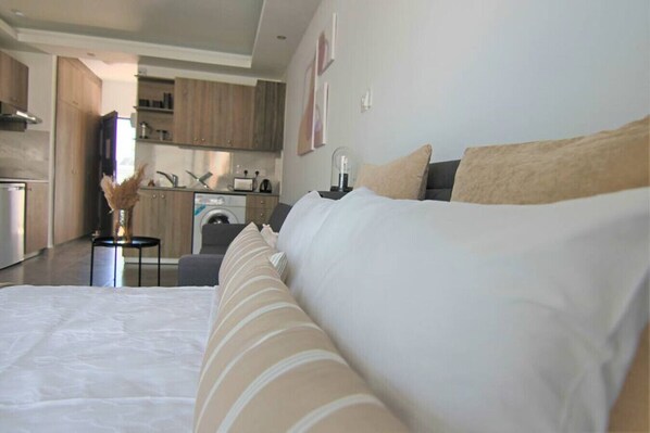 Ein modernes Hotelzimmer mit einem großen Bett, einem kleinen Schreibtisch und einer Küchenzeile im Hintergrund.