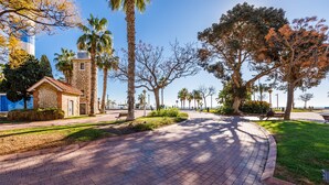 A paved walkway with benches, palm trees, and a small stone building. - A&N Los Angeles (Torre del Mar)