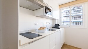 A modern kitchen with white cabinets, a built-in microwave, a sink, and a window with a view of a building. - A&N Los Angeles (Torre del Mar)