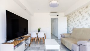 A modern living room with a flat-screen TV, a coffee table, a sofa, and a dining area with chairs and a small plant. - A&N Los Angeles (Torre del Mar)