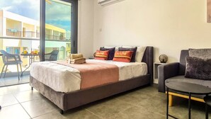 A modern hotel room with a large bed, a chair, and a balcony with a view of buildings. - Phaedrus Living: Seaside Luxury Flat Athina 115 (Paphos)