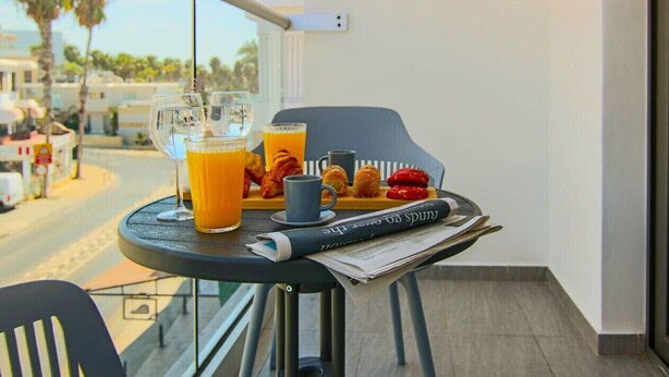 A balcony with a table set for breakfast, including croissants, a cup, and a glass of orange juice. - Phaedrus Living: Seaside Luxury Flat Athina 115 (Paphos)