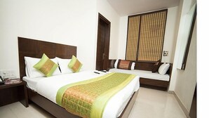 A hotel room with a large bed, a bedside table, a window with blinds, and a wall-mounted TV. - Hotel Sunrise Dx @ Opposite New Delhi Railway Station (New Delhi)