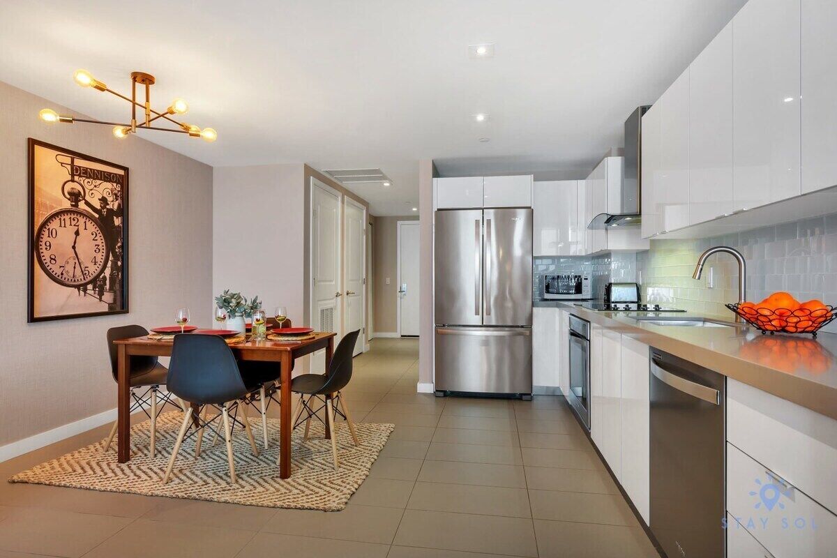 A modern kitchen with stainless steel appliances, a dining area with a wooden table and chairs, and a kitchen island with a sink and countertop.