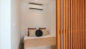 Une chambre à coucher avec un lit, des oreillers, une couverture, un appareil de climatisation et un mur constitué de lattes de bois.
