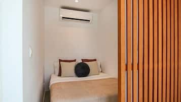 Et soveværelse med en seng, puder, en rund sort pude og en aircondition-enhed på væggen.