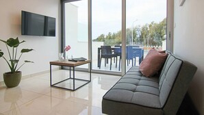 Un salon moderne comprenant un canapé, une table basse, un téléviseur fixé au mur et une grande porte-fenêtre coulissante donnant sur un espace extérieur.