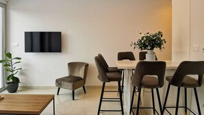Een moderne woonkamer met een flatscreen televisie, een salontafel en een eethoek met stoelen en een tafel.