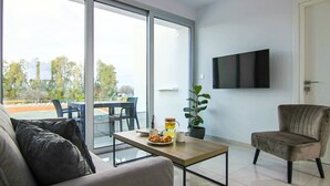 Ein modernes Wohnzimmer mit einer Couch, einem Couchtisch mit Gebäck, einer Topfpflanze und einem an der Wand befestigten Flachbildfernseher.