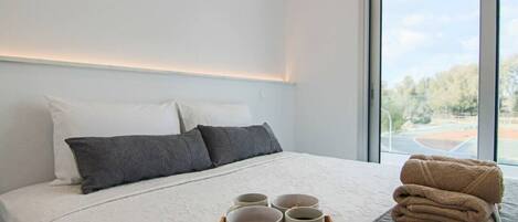 A neatly made bed with pillows, a tray with bowls and a spoon, and a stack of towels.