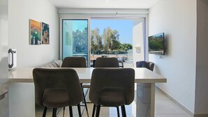 A modern living room with a large glass door leading to a balcony, a dining area with a table and chairs, and a flat-screen TV mounted on the wall. - Phaedrus Living Seaside Executive Flat Harbour 203 (Paphos)