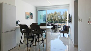 A modern kitchen with a dining area, large windows, and a view of trees. - Phaedrus Living Seaside Executive Flat Harbour 203 (Paphos)